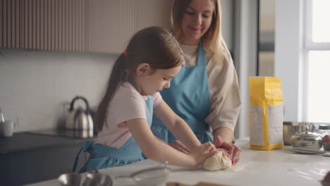 curious-little-girl-is-helping-mother-to-cook-in-kitchen-learning-to-knead-dough-on-table-cooking-pie